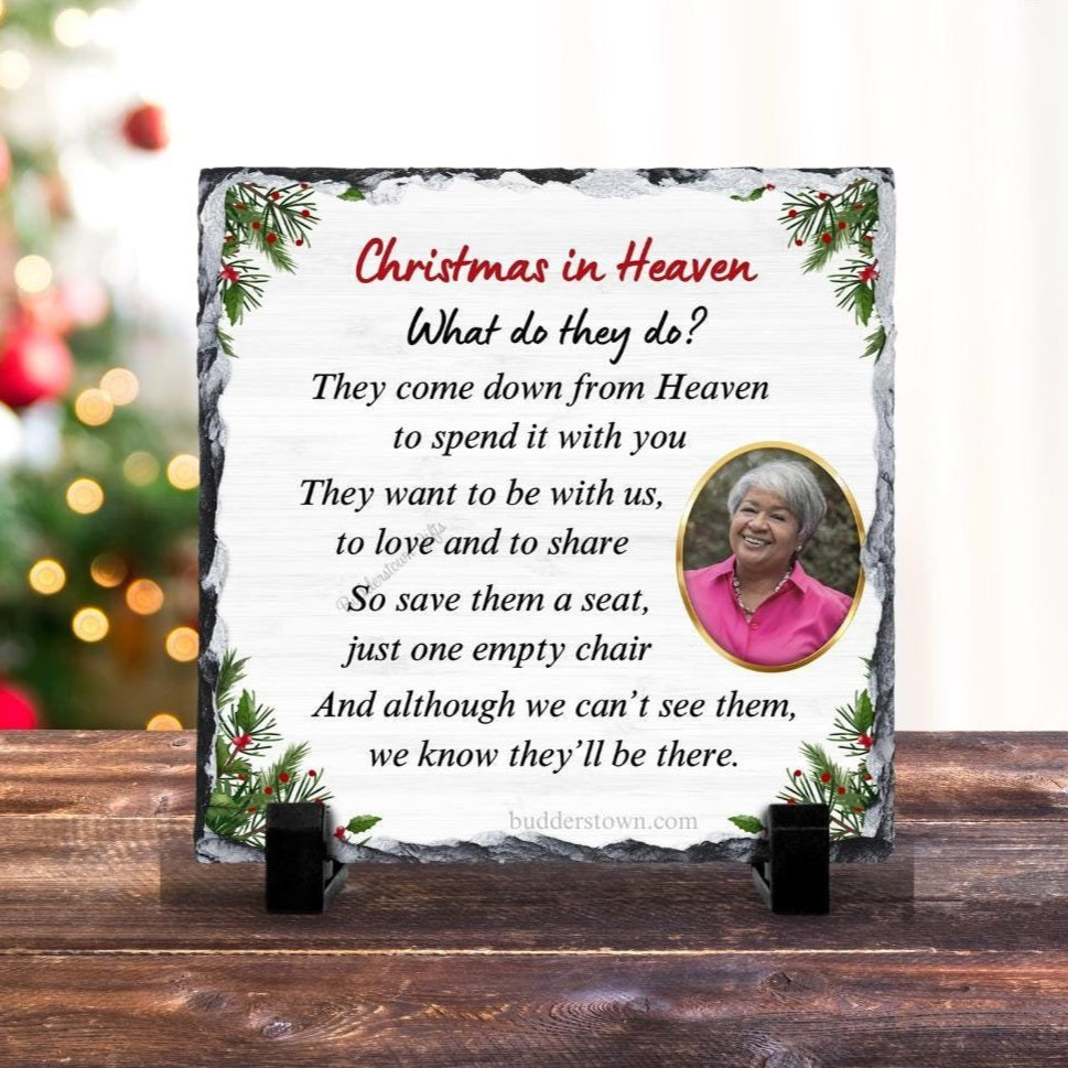 A slate plaque with a Christmas in Heaven theme, featuring a photo of a person and a printed message, displayed on a wooden surface with a Christmas tree in the background.