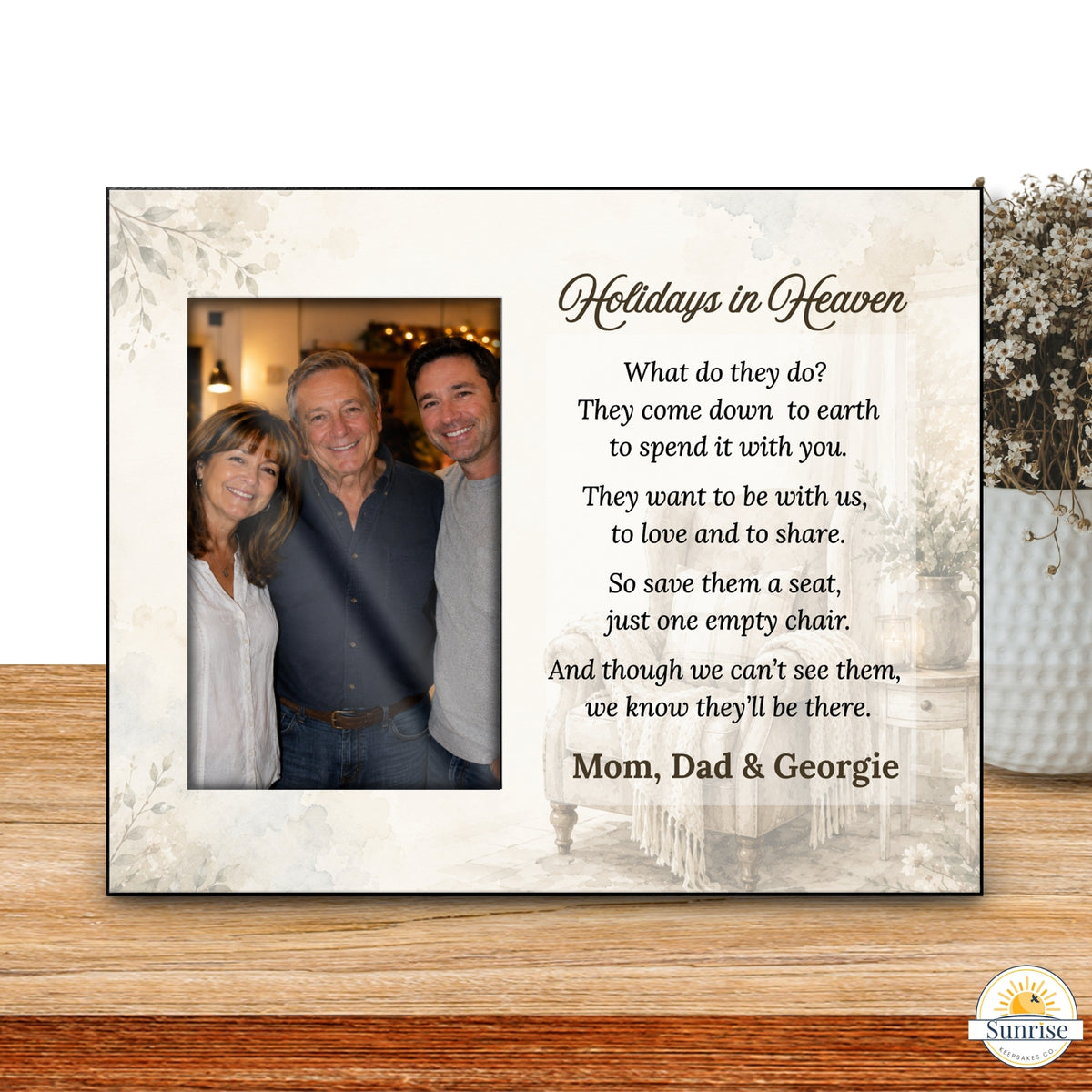 A personalized framed memorial sign displayed on a wooden tabletop. The sign has a cream background with floral corner details, a photo of three people on the left, and a poem titled 'Holidays in Heaven' on the right, personalized with the names 'Mom, Dad & Georgie'.