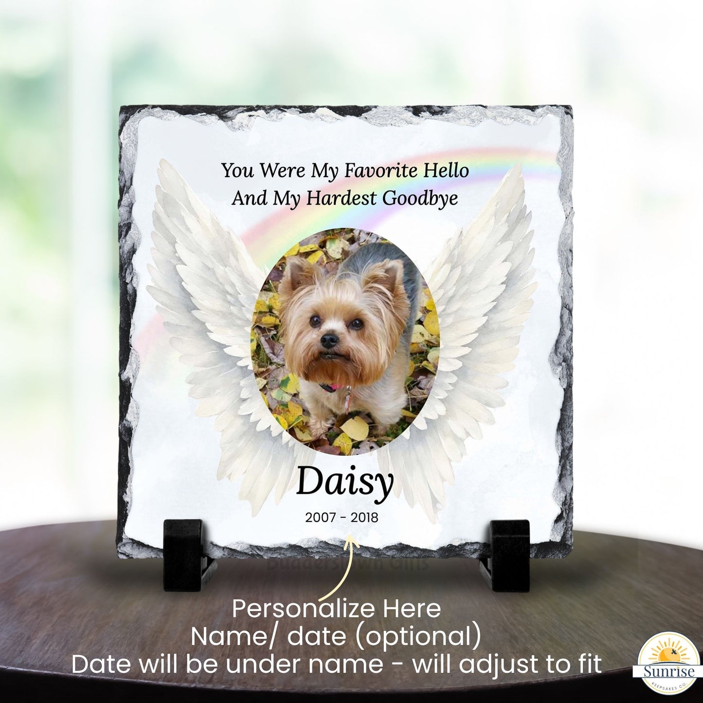 Personalized square slate memorial plaque on a black display stand, featuring a photo of a Yorkshire Terrier dog with white angel wings, a faint rainbow, and the text 'You Were My Favorite Hello And My Hardest Goodbye' and 'Daisy 2007 - 2018'.
