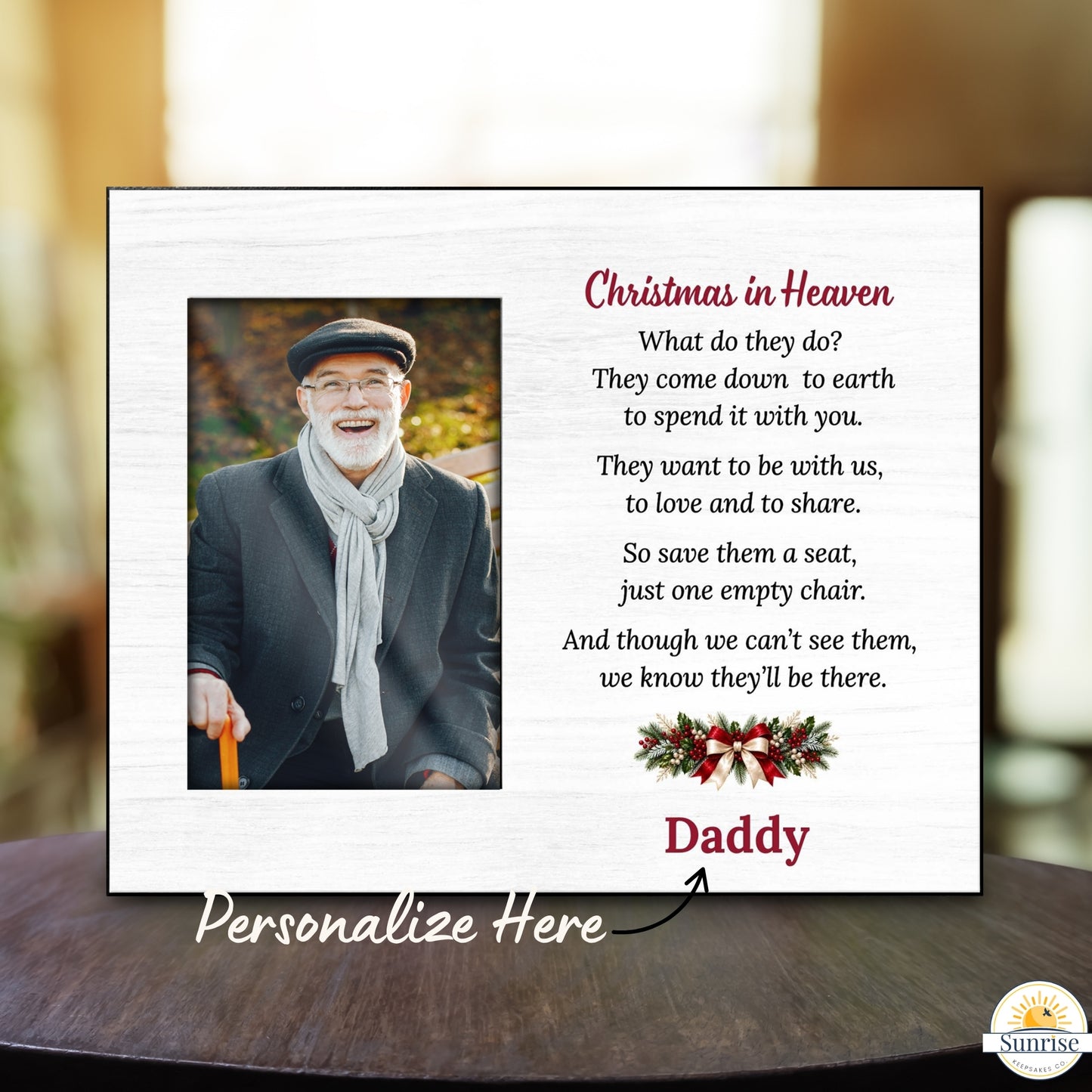 A personalized Christmas in Heaven memorial plaque displayed on a dark wooden table with a blurred indoor background. The white plaque features a photo of a smiling man, a poem, a red 'Daddy' name, and a holiday wreath.