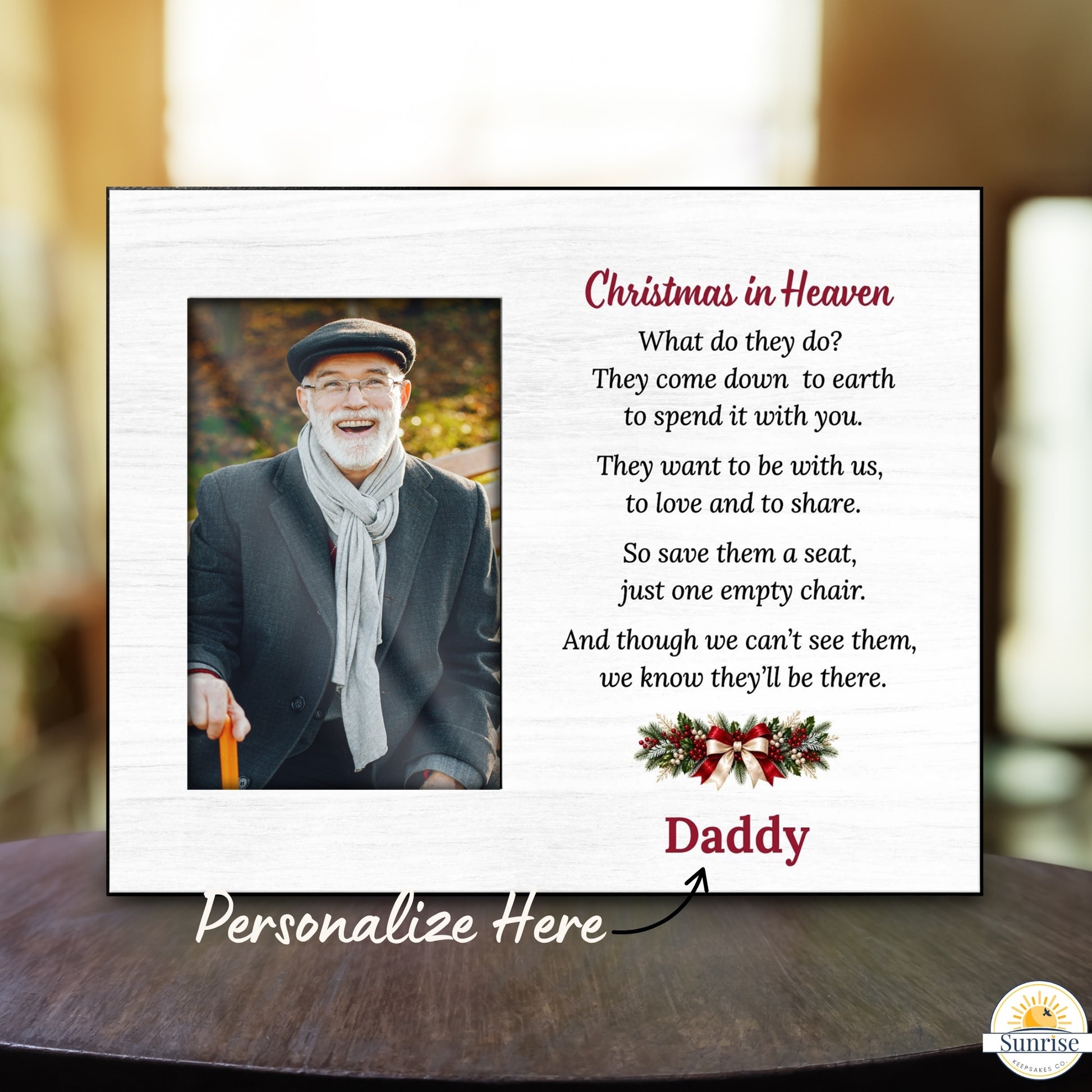 A personalized Christmas in Heaven memorial plaque displayed on a dark wooden table with a blurred indoor background. The white plaque features a photo of a smiling man, a poem, a red 'Daddy' name, and a holiday wreath.