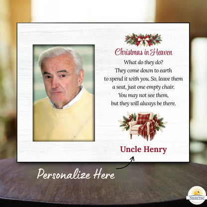 Personalized Christmas in Heaven memorial plaque shown on a dark wooden table with a blurred indoor background. The white plaque features a photo frame, a holiday wreath, a red plaid chair illustration, a poem, and the name 'Uncle Henry' in red.