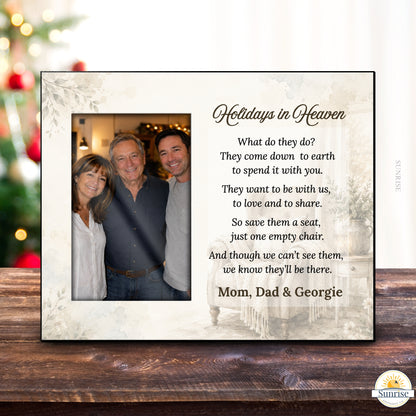 A personalized holiday memorial picture frame displayed on a dark wooden table. The cream-colored frame features a photo of a father and two children on the left, and a poem titled 'Holidays in Heaven' on the right, addressed to 'Mom, Dad & Georgie'.