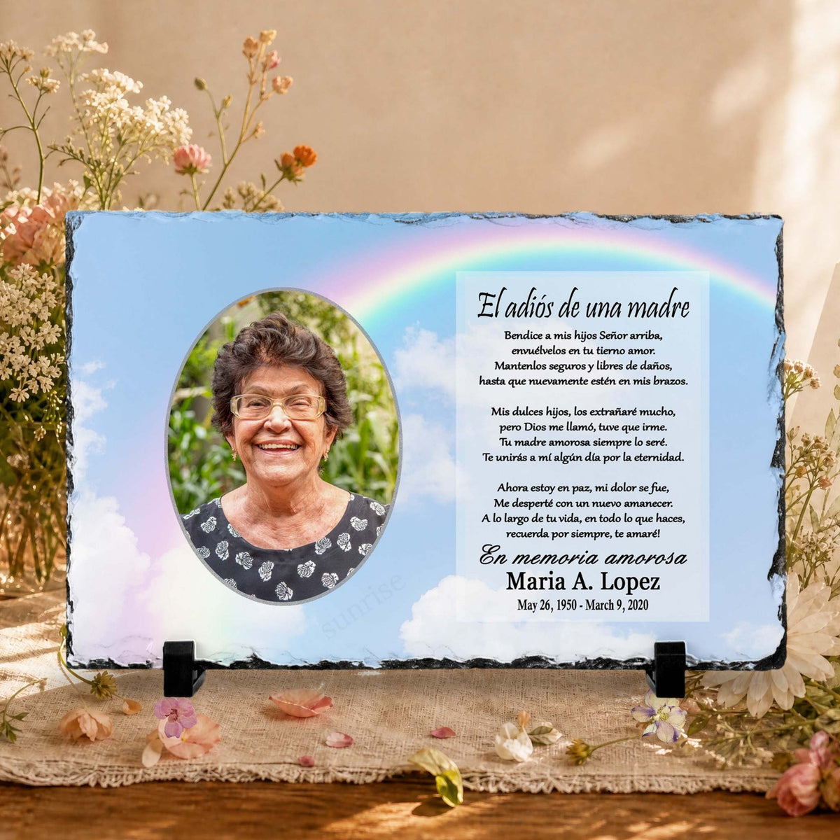 Personalized slate memorial plaque with a photo of a woman and Spanish text honoring her mother, displayed on a wooden surface with flowers and a blurred indoor background.