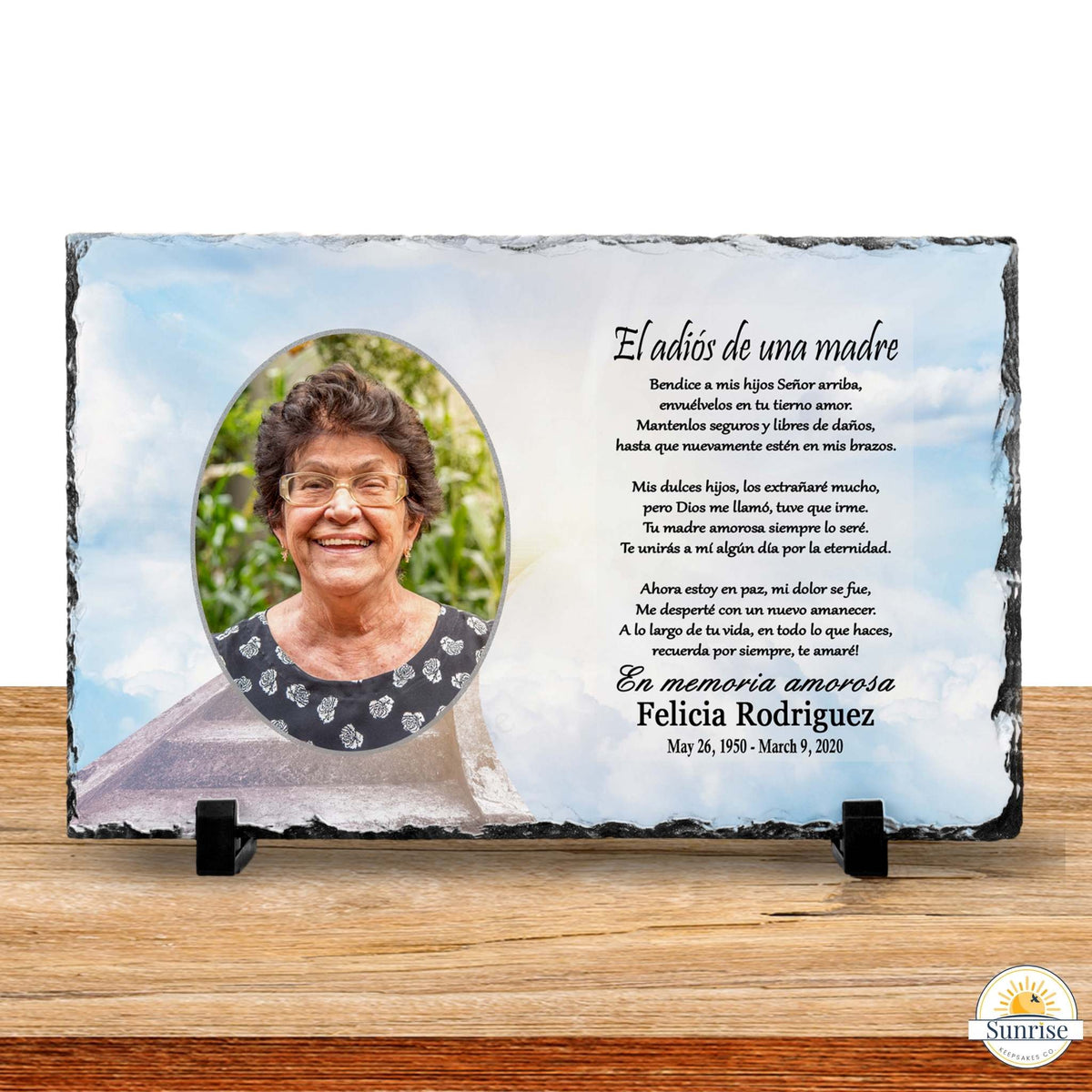 Personalized slate memorial plaque for a mother, featuring a photo of an elderly woman, Spanish remembrance text, and a light blue sky background, displayed on a wooden surface with black stands.